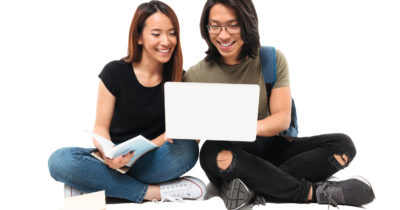Portrait of a happy smiling asian students couple with backpack working on laptop while sitting isolated over white background